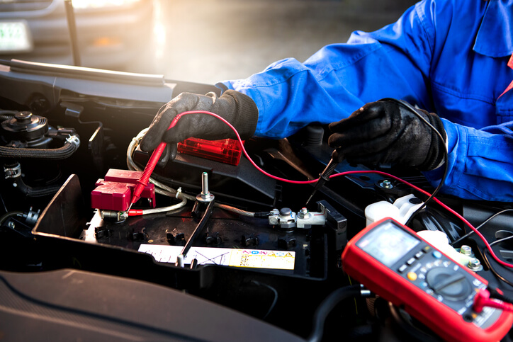 An auto mechanic school in Surrey student testing a car battery with a multimeter during winter diagnostics.