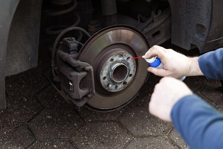 An auto mechanic school trainee applying anti-seize to a wheel hub to prevent future corrosion.