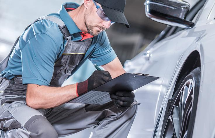 A student reviewing a PDI checklist next to a new vehicle during auto mechanic training