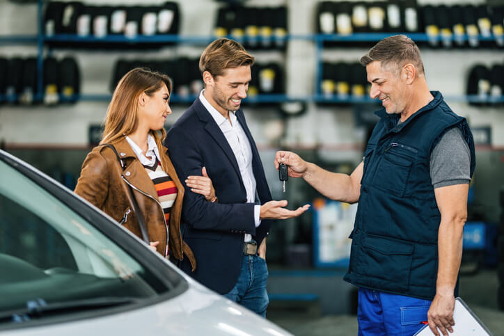 A professional mechanic handing car keys to customers in a clean shop, showing trust built through auto mechanic training.