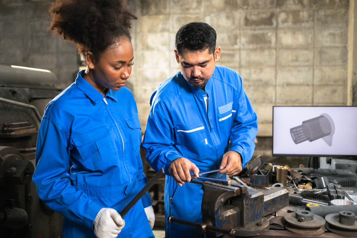 Instructor guiding an aspiring mechanic on proper tool use in a training shop