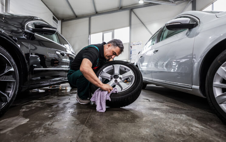 An auto mechanic training student learning eco-friendly tire cleaning techniques during a practical workshop.