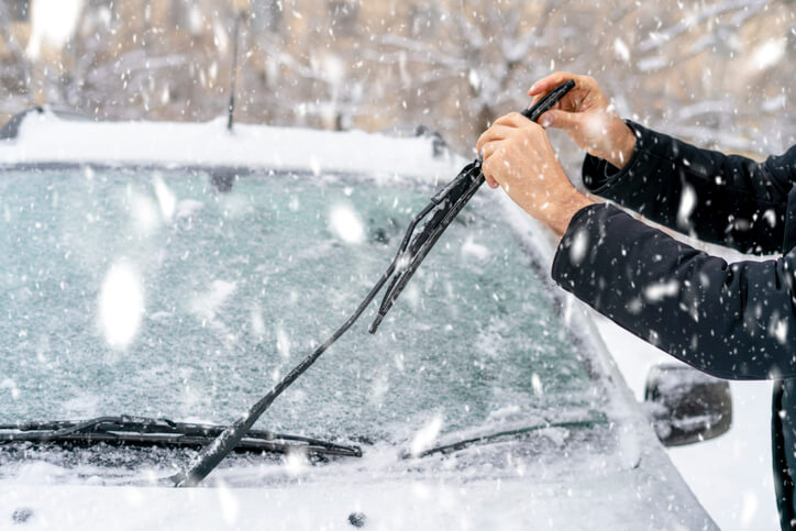 A technician replacing a winter-rated wiper blade on a snow-covered windshield as part of auto mechanic training.
