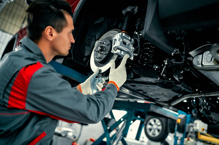A learner inspecting a brake system in a garage setting as part of auto mechanic training for winter maintenance.