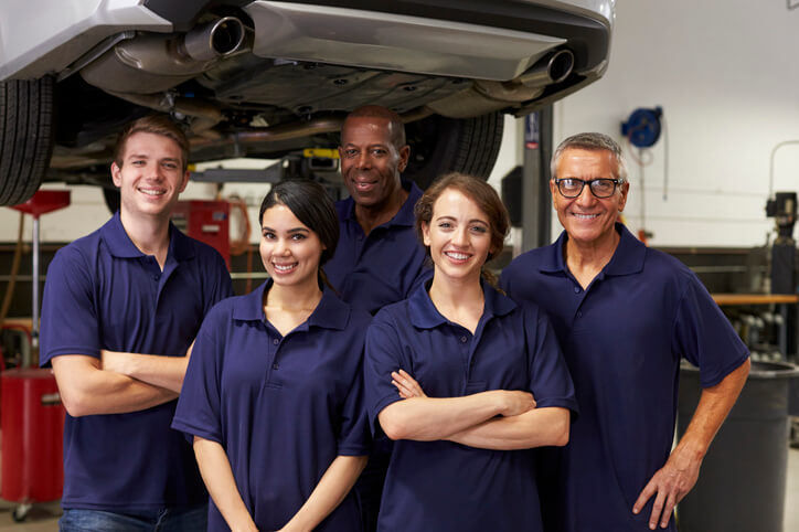 A group of students in hybrid and electrical mechanic training stand together in a workshop, gaining hands-on experience in automotive repair.