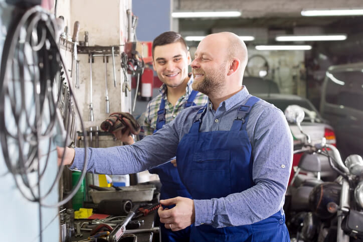 An auto mechanic school in Surrey, an instructor and a student working together in a repair shop.