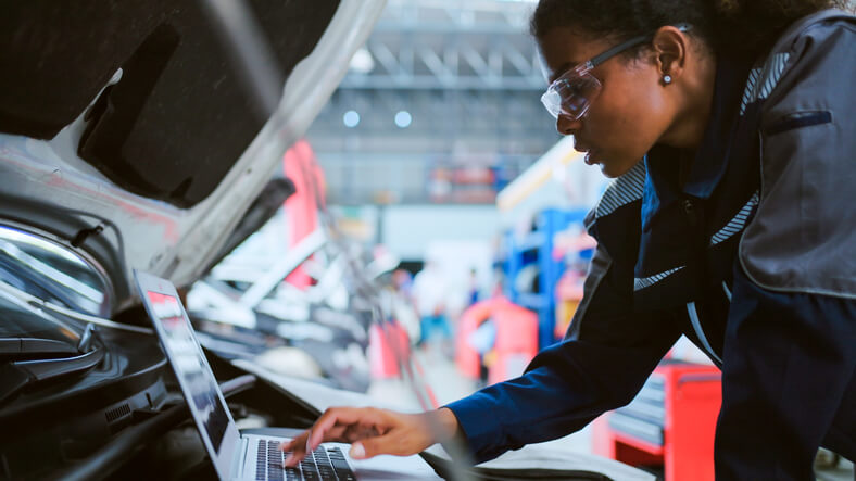 A student at an auto mechanic school in Surrey using a laptop to diagnose an electrical issue under the hood.