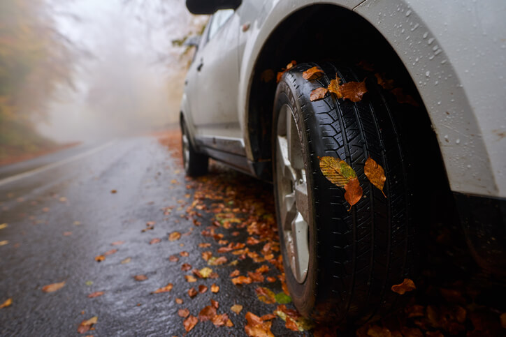 A car on a wet, leaf-covered road used during an auto mechanic training road test to check alignment and traction issues.