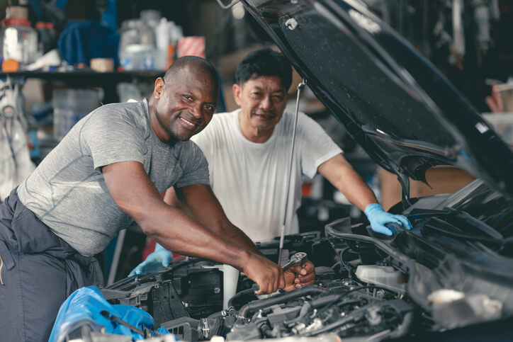 A pair of students learning hands-on repair skills at an auto mechanic school workshop