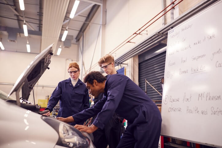 An automotive training: Hands-on training at a vehicle workstation, with students in uniforms performing diagnostics.