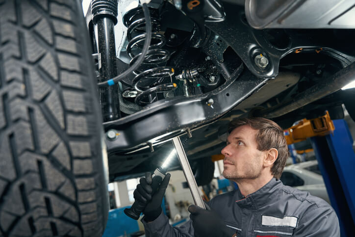 An auto mechanic training graduate inspecting a vehicle suspension for vibration issues