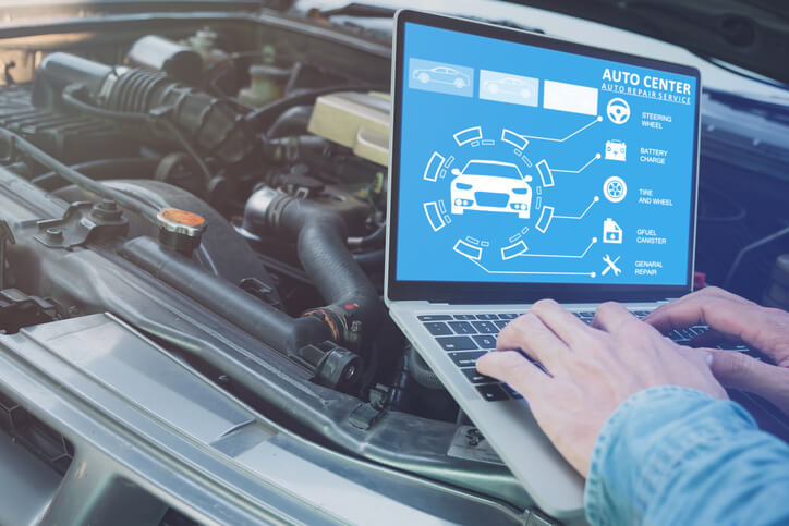 An auto mechanic school student running digital diagnostics on a vehicle engine using advanced software.