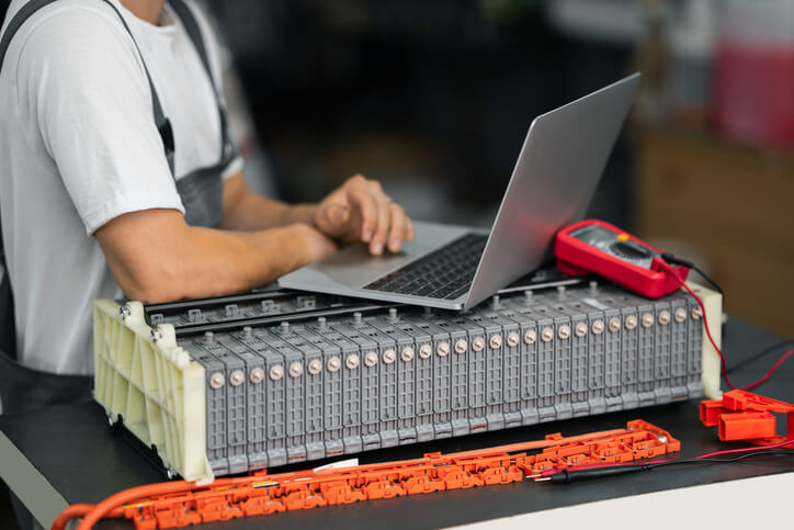 An auto mechanic school student testing an electric vehicle battery using laptop diagnostics.