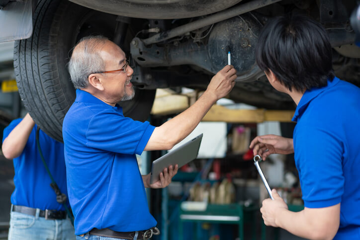 An instructor guiding a student at an auto mechanic school through a brake system inspection to identify pedal-feel problems.