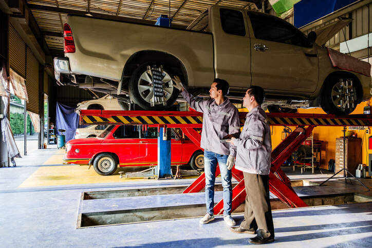 Two trainees at an auto mechanic school practicing safe lifting techniques in the shop.