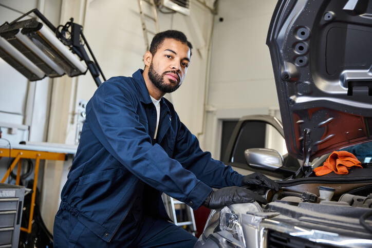 An Automotive service technician program student concentrating on a complex vehicle repair in a busy service center, working methodically through an unfamiliar issue