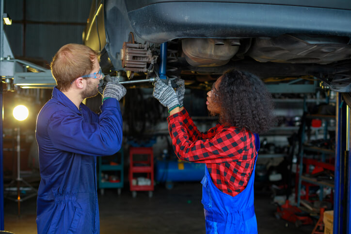 A pair of automotive service technician program graduates working together on scheduled vehicle repairs in a shop