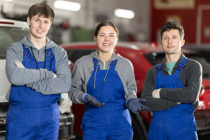 A trio of automotive service technician program students posing together in a training garage.