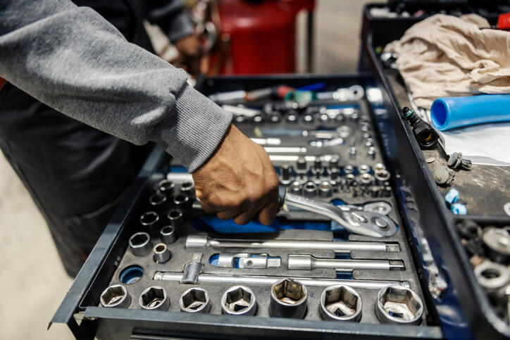 A student at an auto mechanic school selecting essential hand tools from a toolbox.