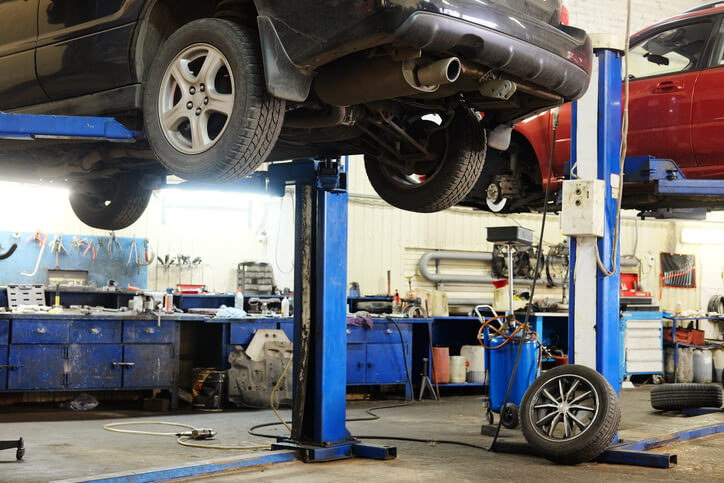 An image of an auto shop, cars ready for inspection as they are lifted, as explored in auto mechanic training