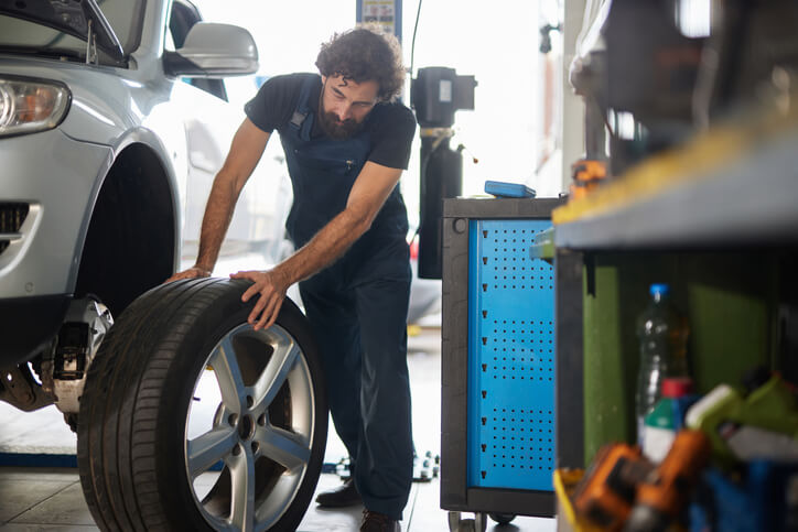 An auto mechanic school graduate changing a tire in a garage, showing hands-on skills developed through automotive school training.