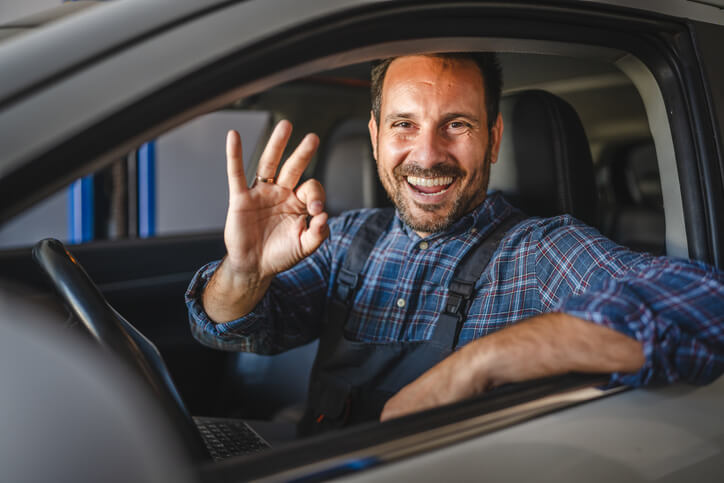 A student in auto mechanic school test-driving a car while listening for engine feedback.