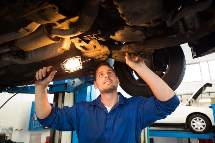 A mechanic shining a torch under a car while applying critical thinking to inspect and diagnose mechanical issues.