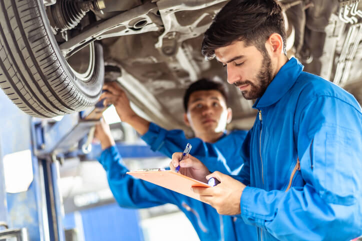 An ATC instructor showing a student how to detect vibration in a suspension component.