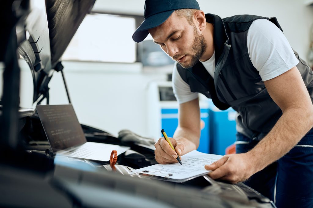 Auto mechanic performing an under-hood inspection checklist during vehicle service