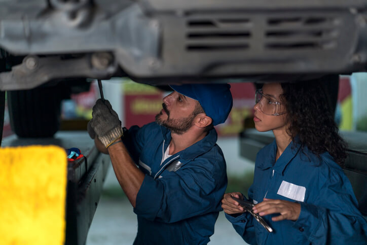 An automotive instructor teaching students safe diagnostic procedures inside a training workshop