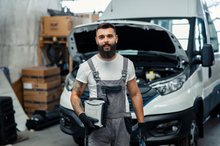 An auto technician wearing protective gloves and safety gear inside a professional automotive workshop