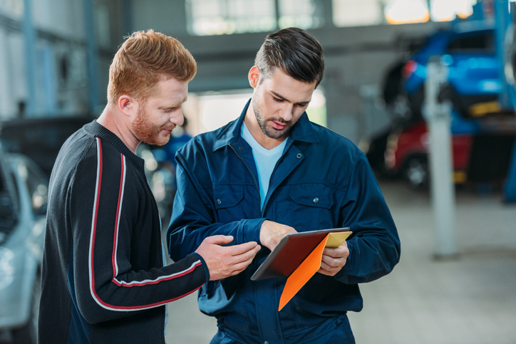 Auto mechanic explaining repair results to a customer using a digital tablet.