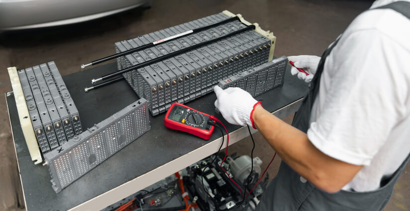 Technician testing an EV auxiliary battery with a digital multimeter