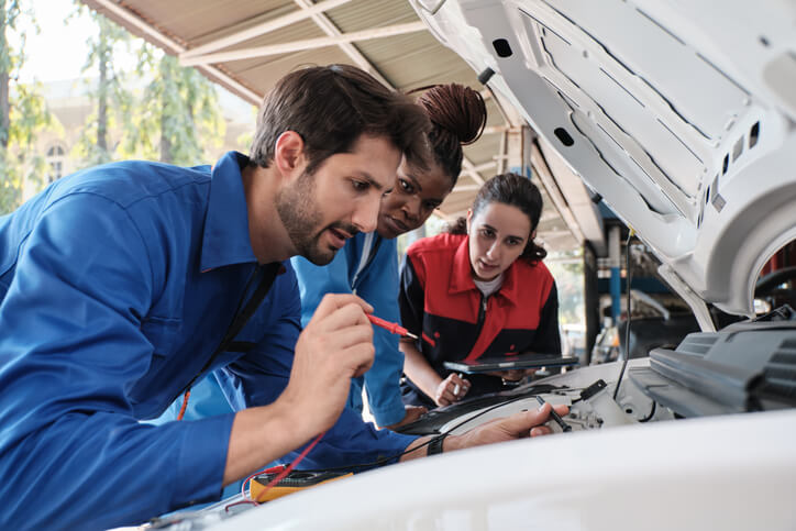 A group of automotive students practising how to charge a car battery during mechanic training.