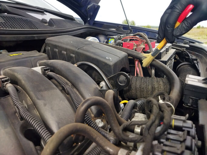 A technician showing how to clean battery terminal corrosion from a car battery terminal using a wire brush