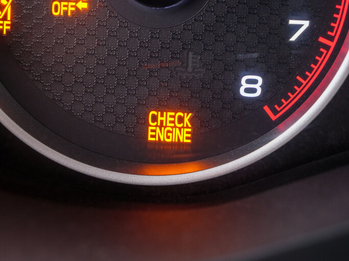 A vehicle dashboard showing a check engine light triggered by a fault