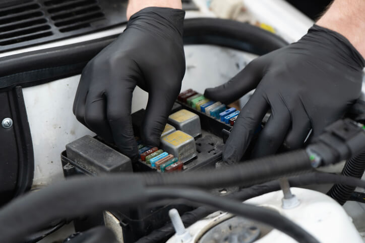 A mechanic is inspecting a fuse box while isolating a parasitic draw during electrical diagnostics