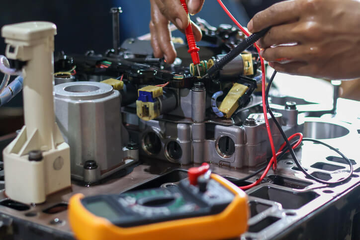 A technician testing a VVT solenoid during variable valve timing diagnosis using a multimeter