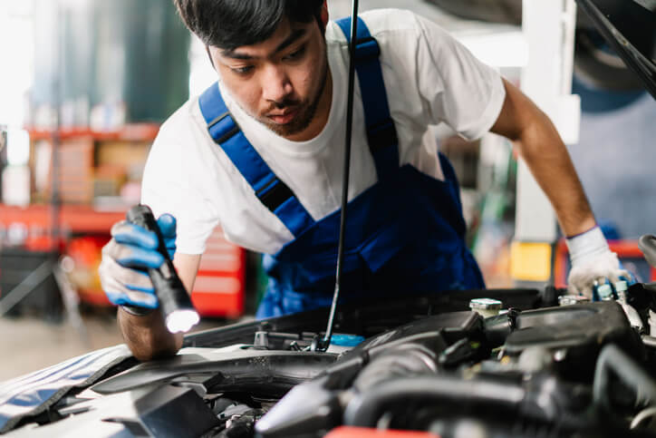 An automotive student checking belt tension during hands-on vehicle maintenance training.