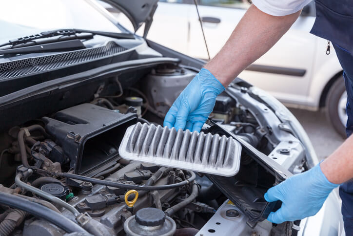 A mechanic is inspecting a dirty engine air filter inside the vehicle's engine bay