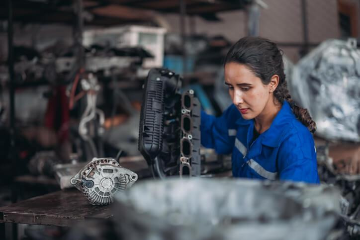 An automotive technician is inspecting hybrid electrical components alongside a gasoline engine assembly