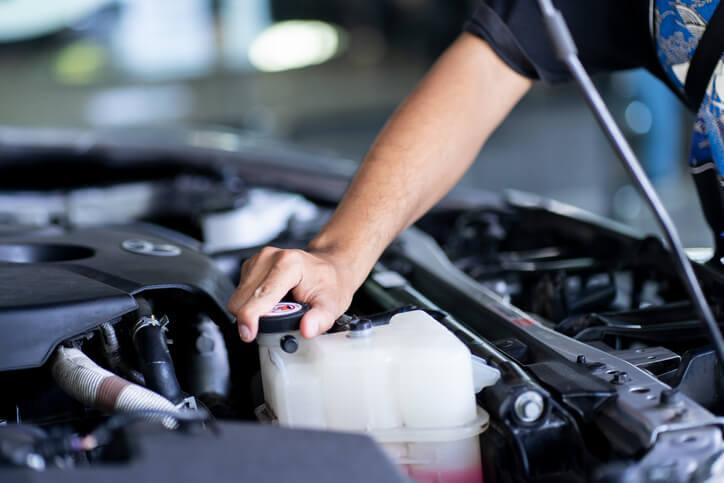 A technician checking coolant levels and radiator components in a vehicle