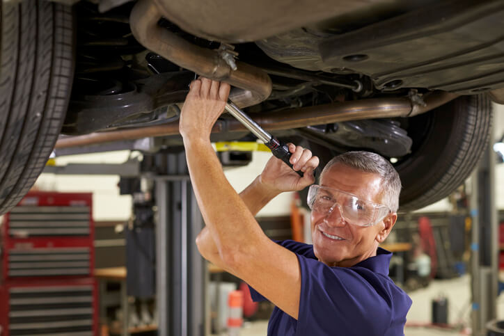 An automotive student inspecting suspension components on a vehicle lift