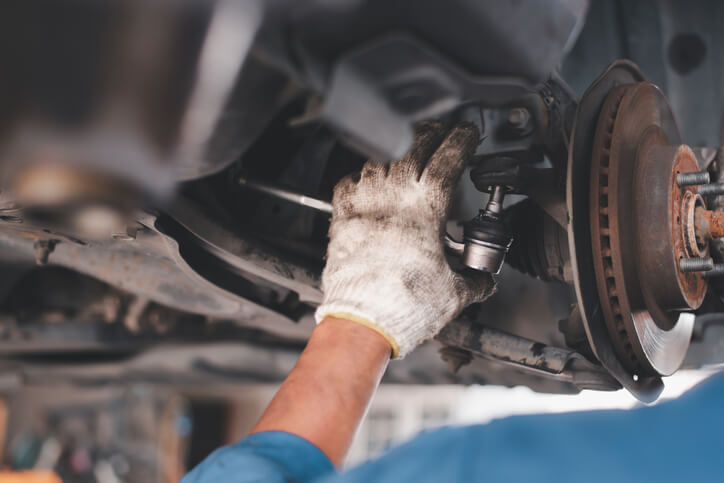Technician checking a vehicle ball joint for excessive movement on a vehicle lift