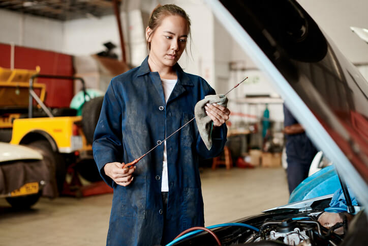 An automotive student inspecting milky oil on an engine dipstick