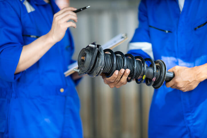 Technician examining a shock absorber for signs of wear on a vehicle lift