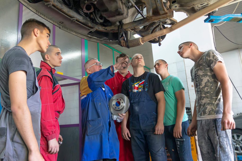 An instructor demonstrating suspension component inspection to automotive students