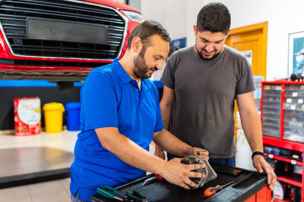 Instructor explaining the purpose of a car alternator in an auto mechanic training lab