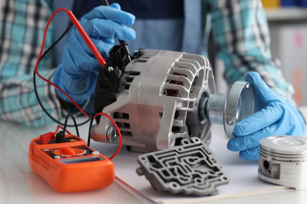 Automotive student testing a car alternator with a digital multimeter during charging system diagnostics