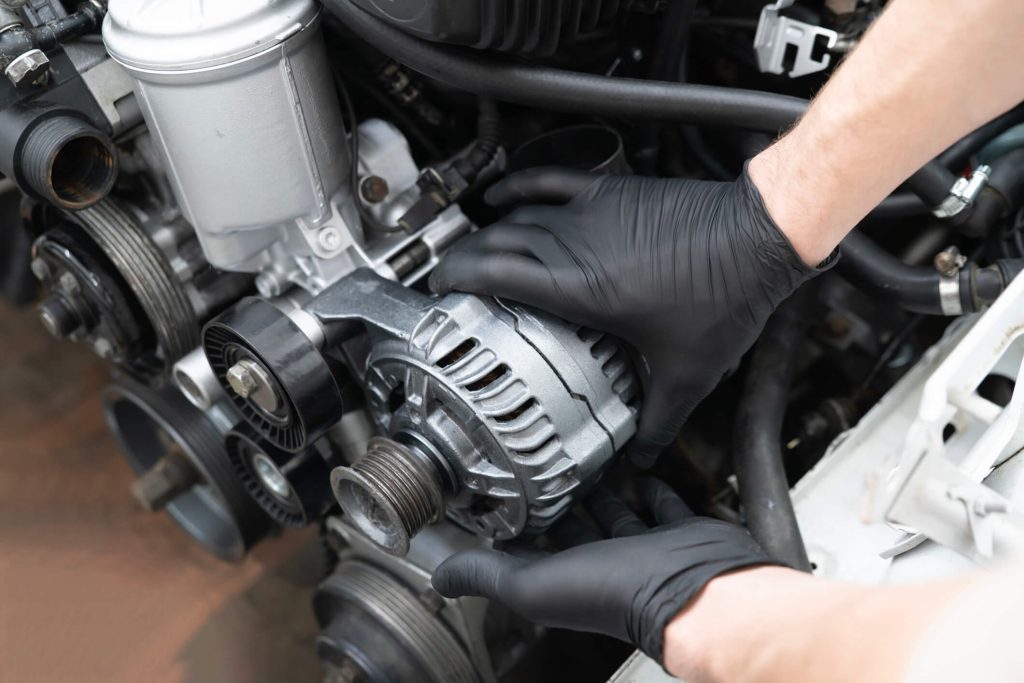 Student inspecting an automotive alternator and drive belt on a vehicle engine